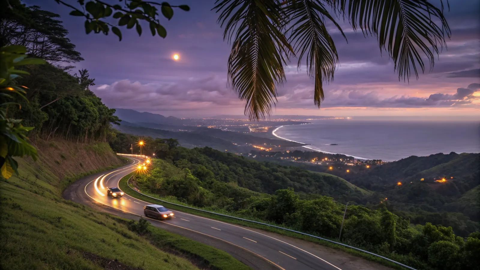 Winding road descending through green hills toward the coast and the lights of Jacó at dusk